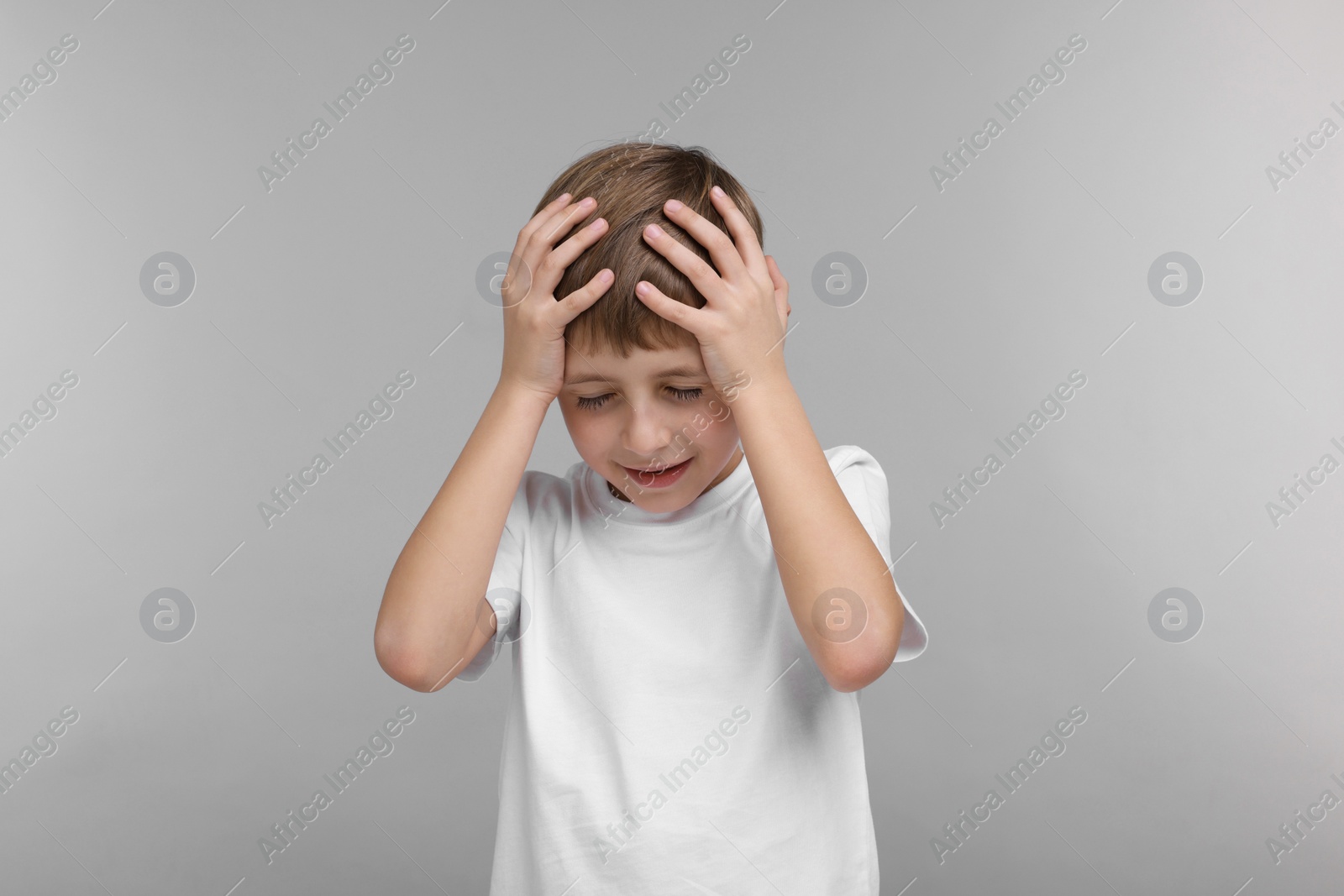 Photo of Little boy suffering from headache on grey background