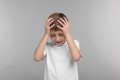 Photo of Little boy suffering from headache on grey background