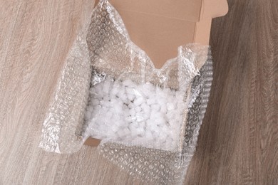 Photo of Bubble wrap and foam peanuts in cardboard box on wooden table, above view