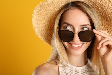 Beautiful woman in stylish sunglasses on yellow background, closeup. Space for text