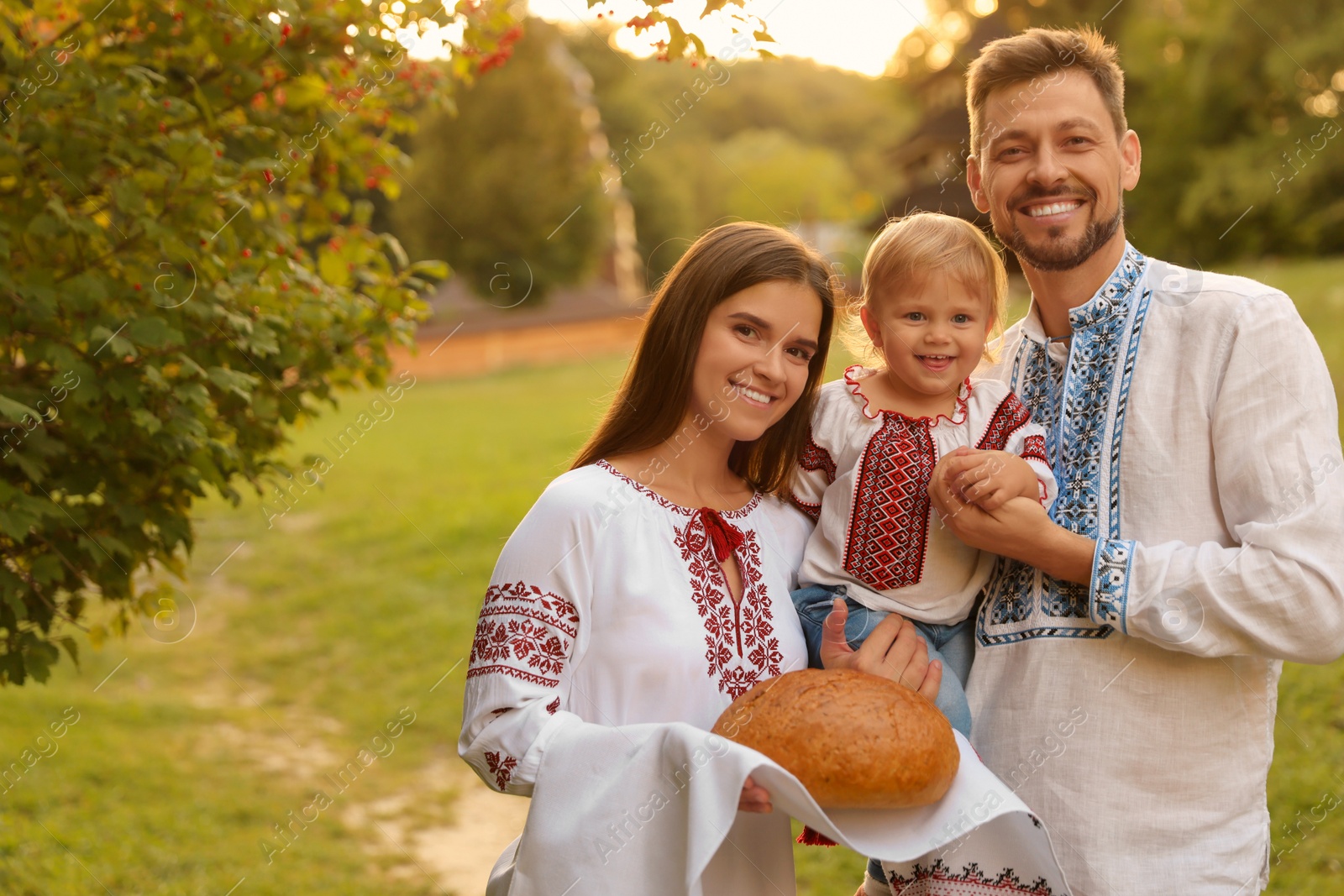 Photo of Happy cute family in embroidered Ukrainian shirts with korovai bread on sunny day. Space for text