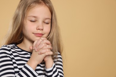Photo of Girl with clasped hands praying on beige background, space for text