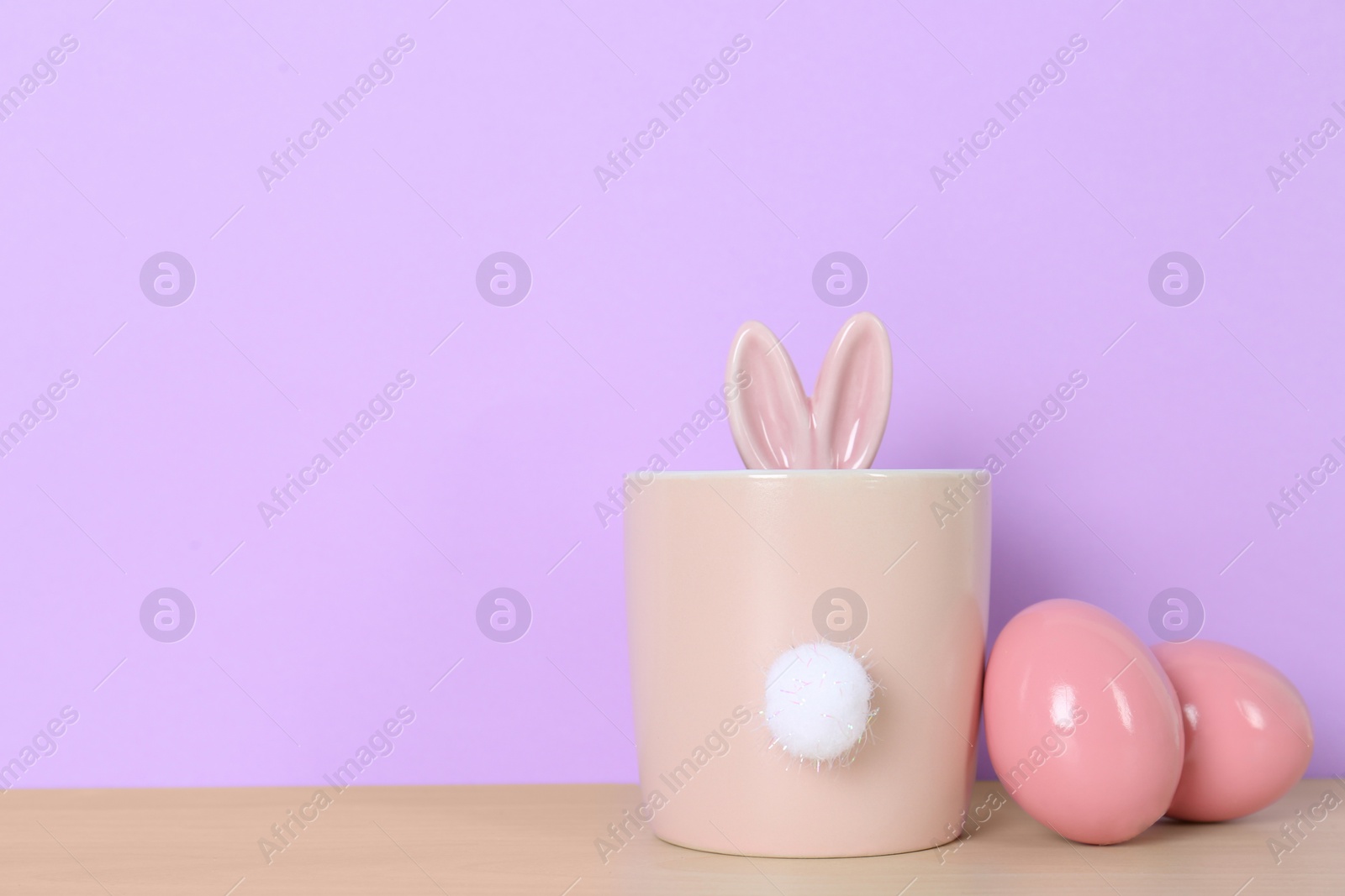 Photo of Dyed eggs near cute pot with Easter bunny ears and tail on table against color background, space for text