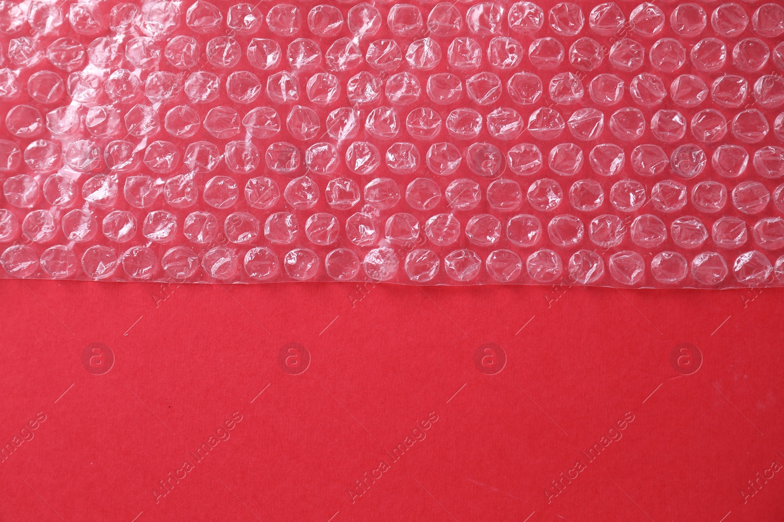 Photo of Transparent bubble wrap on red background, top view. Space for text