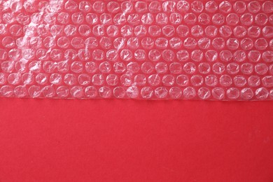 Transparent bubble wrap on red background, top view. Space for text