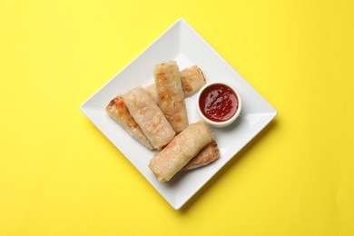 Photo of Fried spring rolls and sauce on yellow table, top view