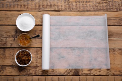 Roll of baking parchment paper with different ingredients on wooden table, flat lay. Space for text