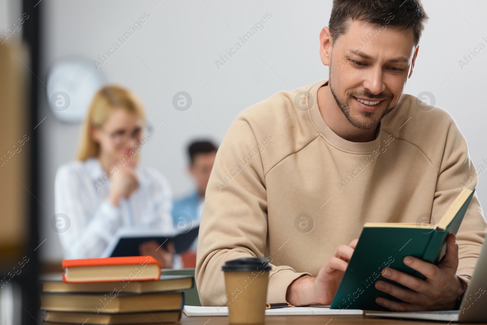 Photo of Man reading book at table in library