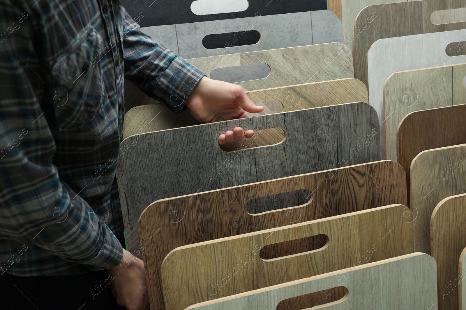 Photo of Man choosing wooden flooring among different samples in shop, closeup