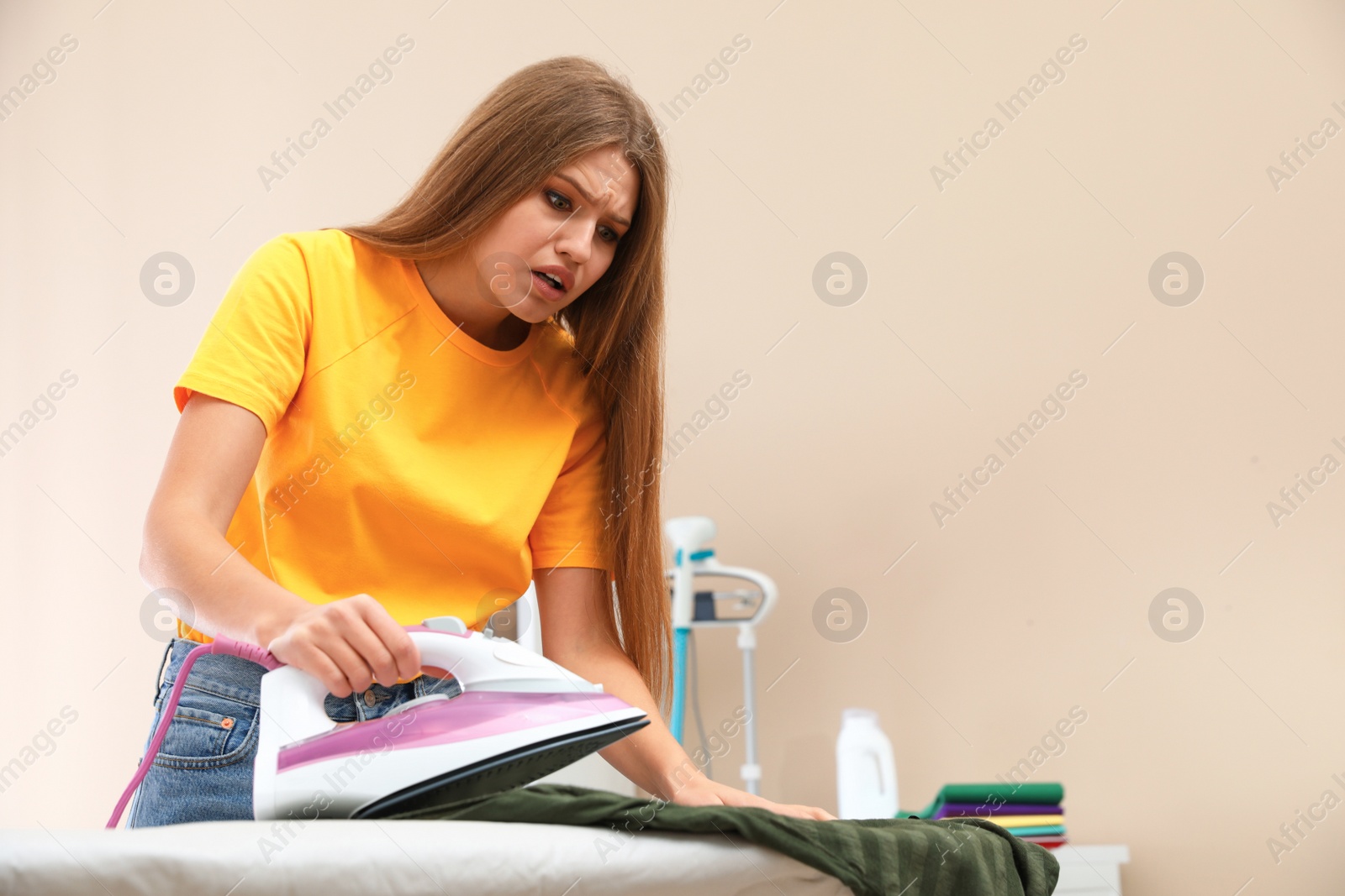 Photo of Emotional woman ironing shirt on board at home. Space for text