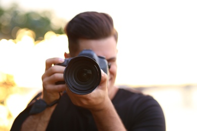 Photographer taking picture with professional camera in countryside, focus on lens