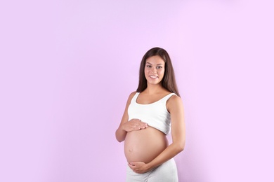 Happy pregnant woman posing on color background