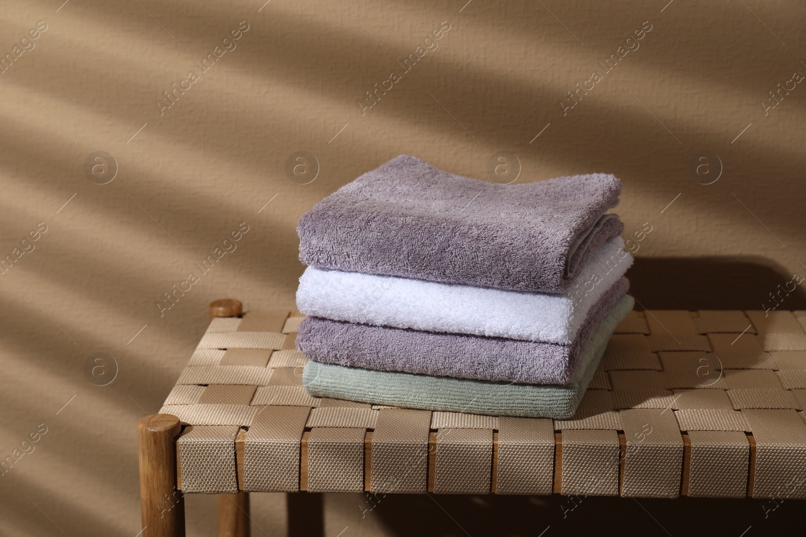 Photo of Stacked terry towels on wicker bench near beige wall