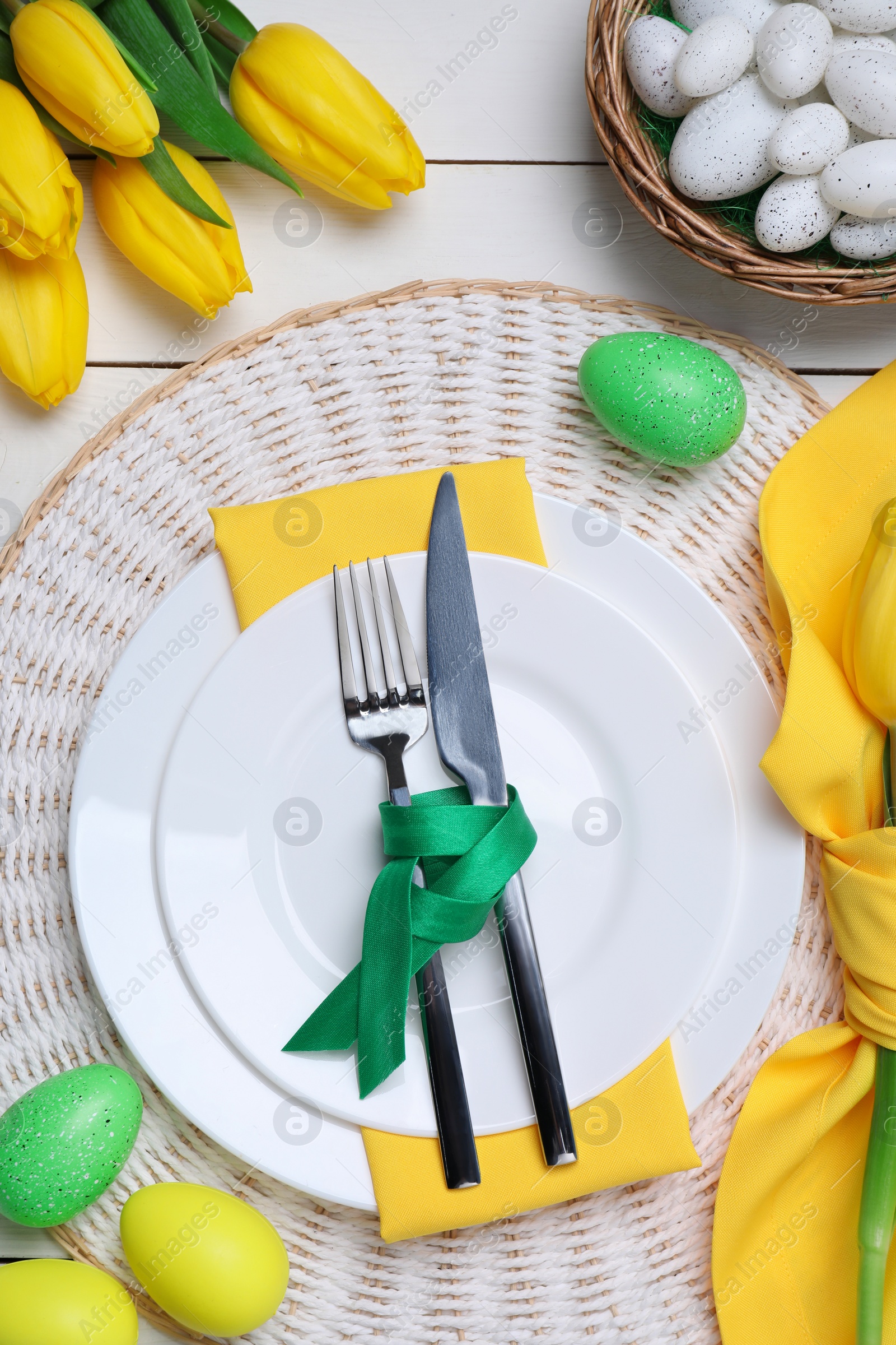 Photo of Festive table setting with painted eggs and tulips, flat lay. Easter celebration