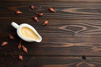 Tasty sauce in gravy boat, small onion bulbs and spice on wooden table, flat lay. Space for text