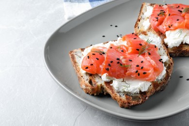Photo of Delicious sandwiches with cream cheese, salmon and black sesame seeds on light grey table, closeup