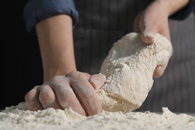 Making bread. Woman kneading dough at table on dark background, closeup