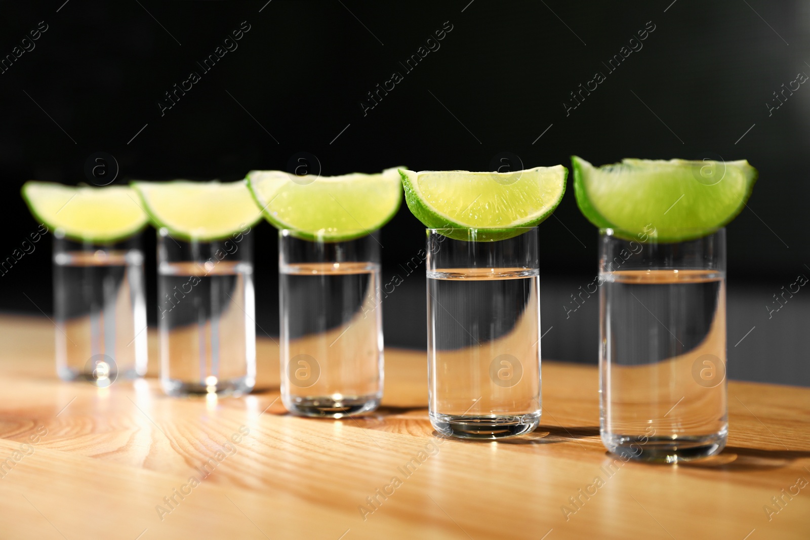 Photo of Vodka shots and lime slices on wooden bar counter