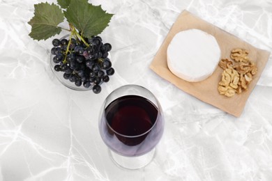 Photo of Glass of red wine and snacks served on white marble table, above view
