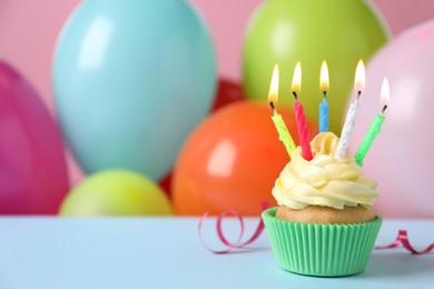 Photo of Birthday cupcake with burning candles and streamer on light blue table against color balloons. Space for text
