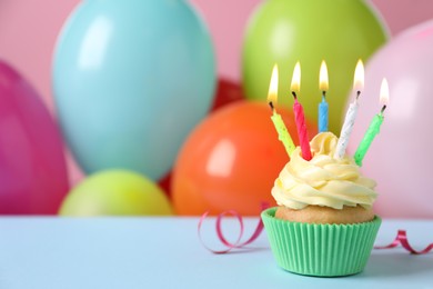 Birthday cupcake with burning candles and streamer on light blue table against color balloons. Space for text