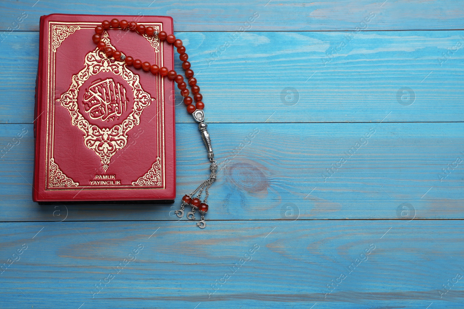 Photo of Muslim prayer beads and Quran on light blue wooden table, top view. Space for text
