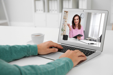 Image of Man using laptop at table for online consultation with psychologist via video chat, focus on screen