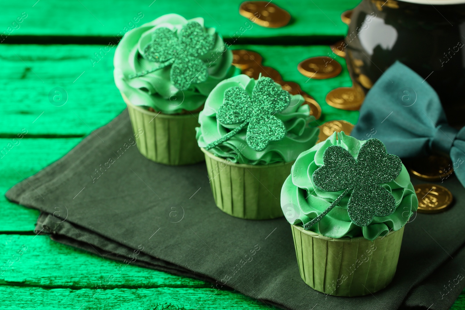 Image of St. Patrick's day. Tasty cupcakes with clover leaf toppers and cream on green wooden table, closeup