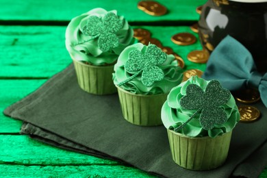 Image of St. Patrick's day. Tasty cupcakes with clover leaf toppers and cream on green wooden table, closeup