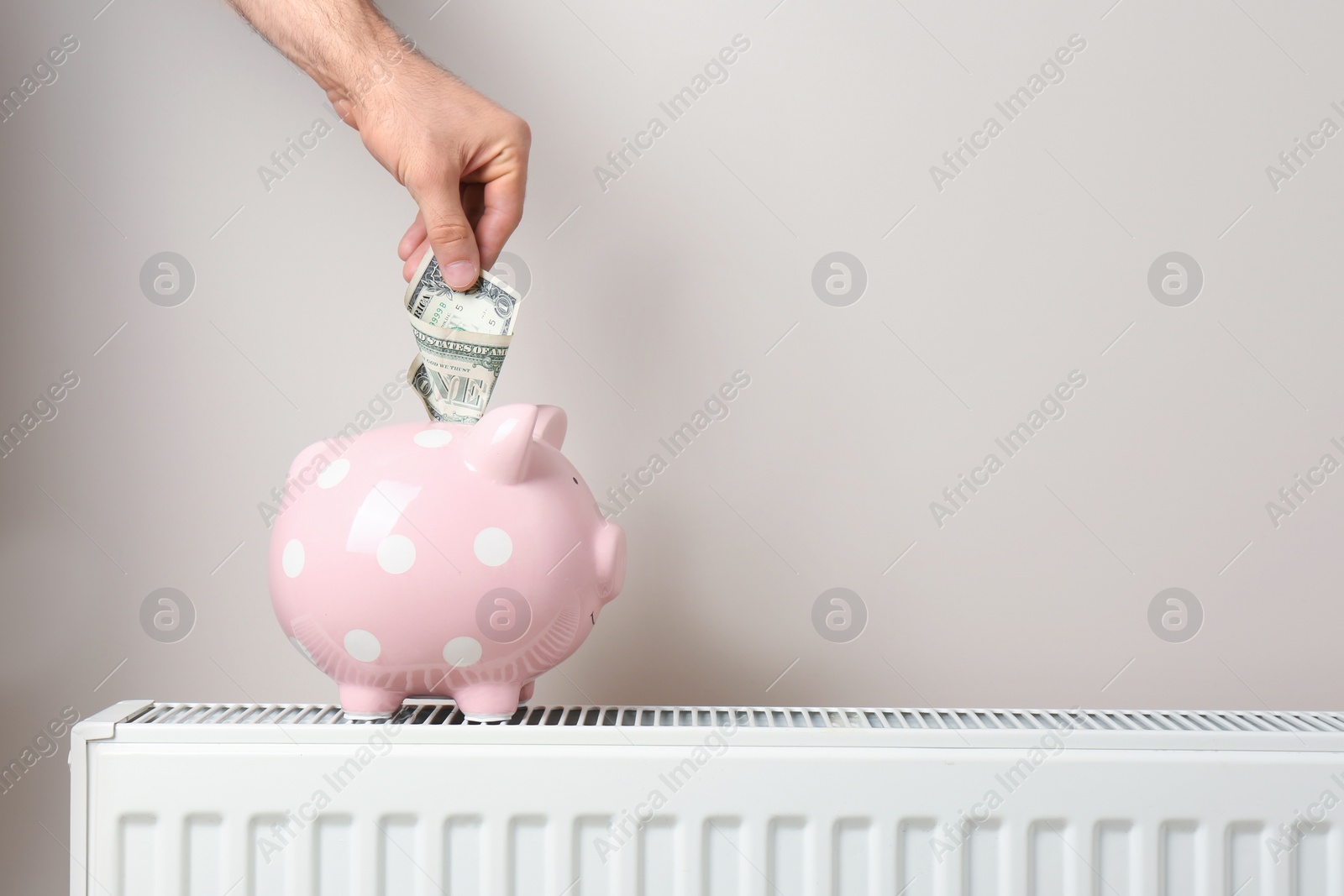 Photo of Man inserting money into piggy bank on heating radiator against color background. Space for text