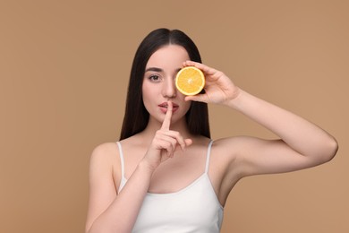 Photo of Beautiful young woman with piece of orange showing hush gesture on beige background