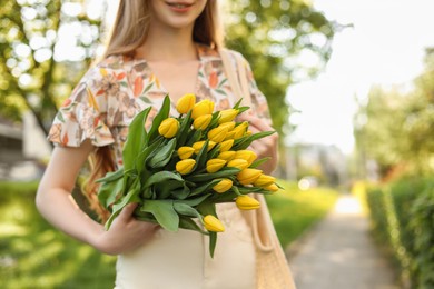 Photo of Teenage girl with bouquet of yellow tulips in park on sunny day, closeup