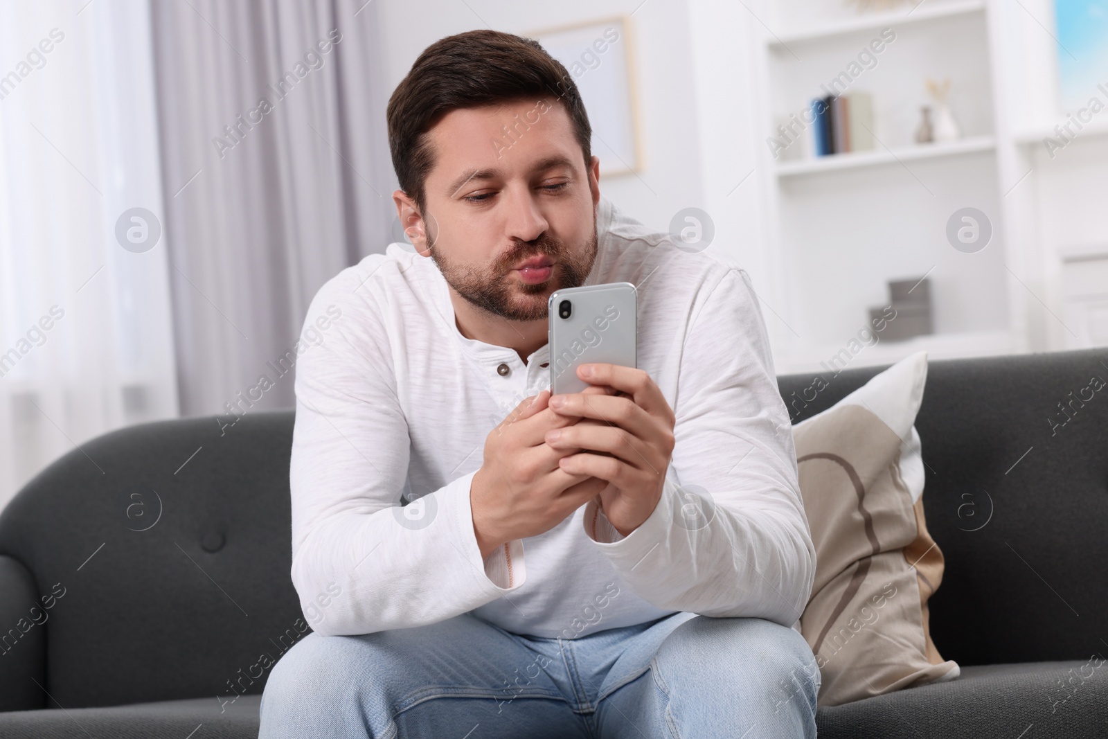 Photo of Man blowing kiss during video chat via smartphone at home. Long-distance relationship