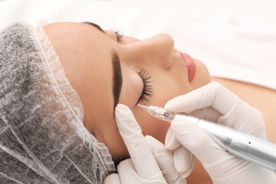 Photo of Young woman undergoing procedure of permanent eye makeup in tattoo salon, closeup