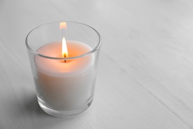 Photo of Beautiful burning wax candle in glass on table