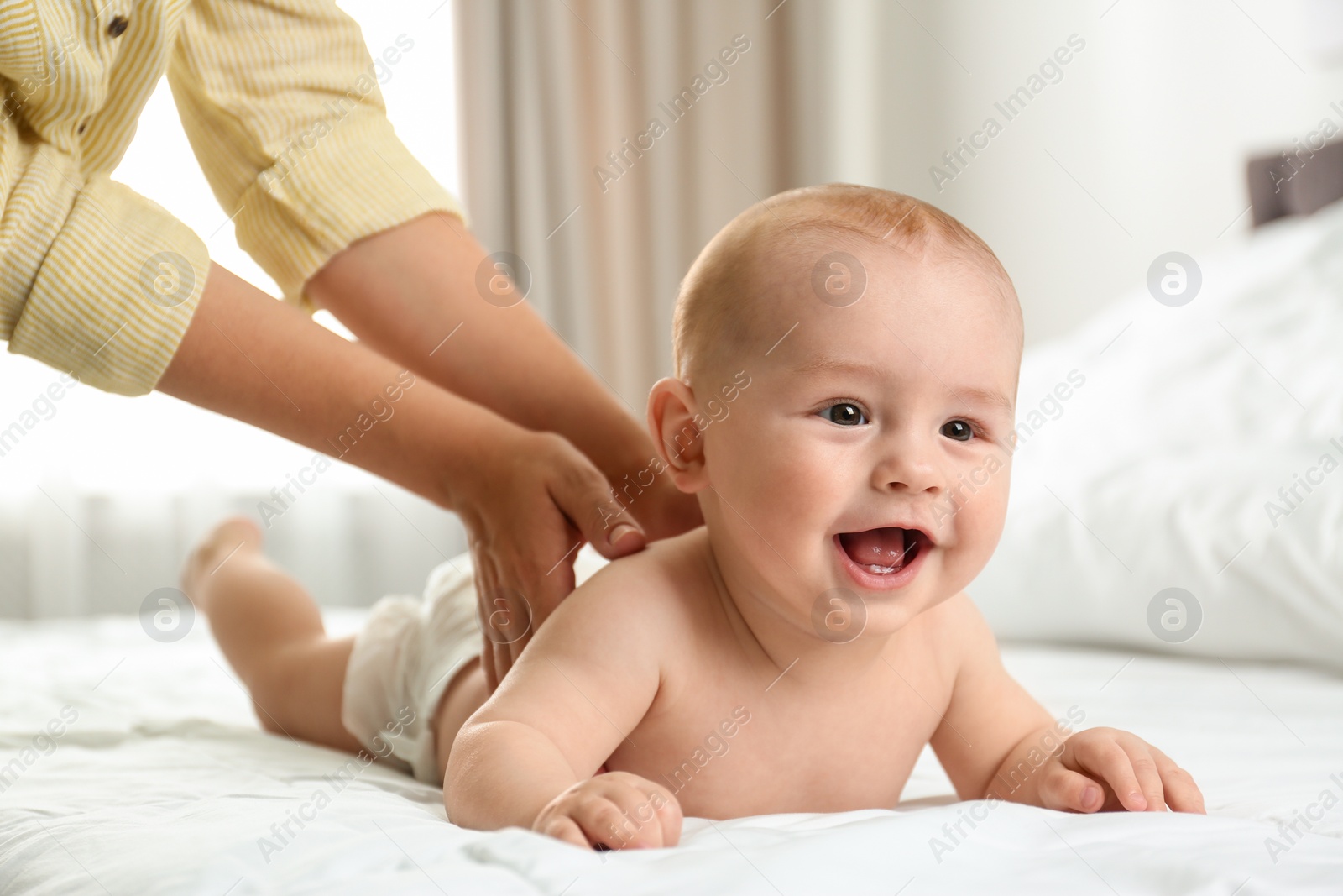 Photo of Young woman massaging cute little baby on bed indoors