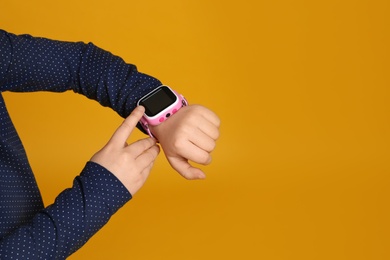 Photo of Little girl with smart watch on yellow background, closeup. Space for text