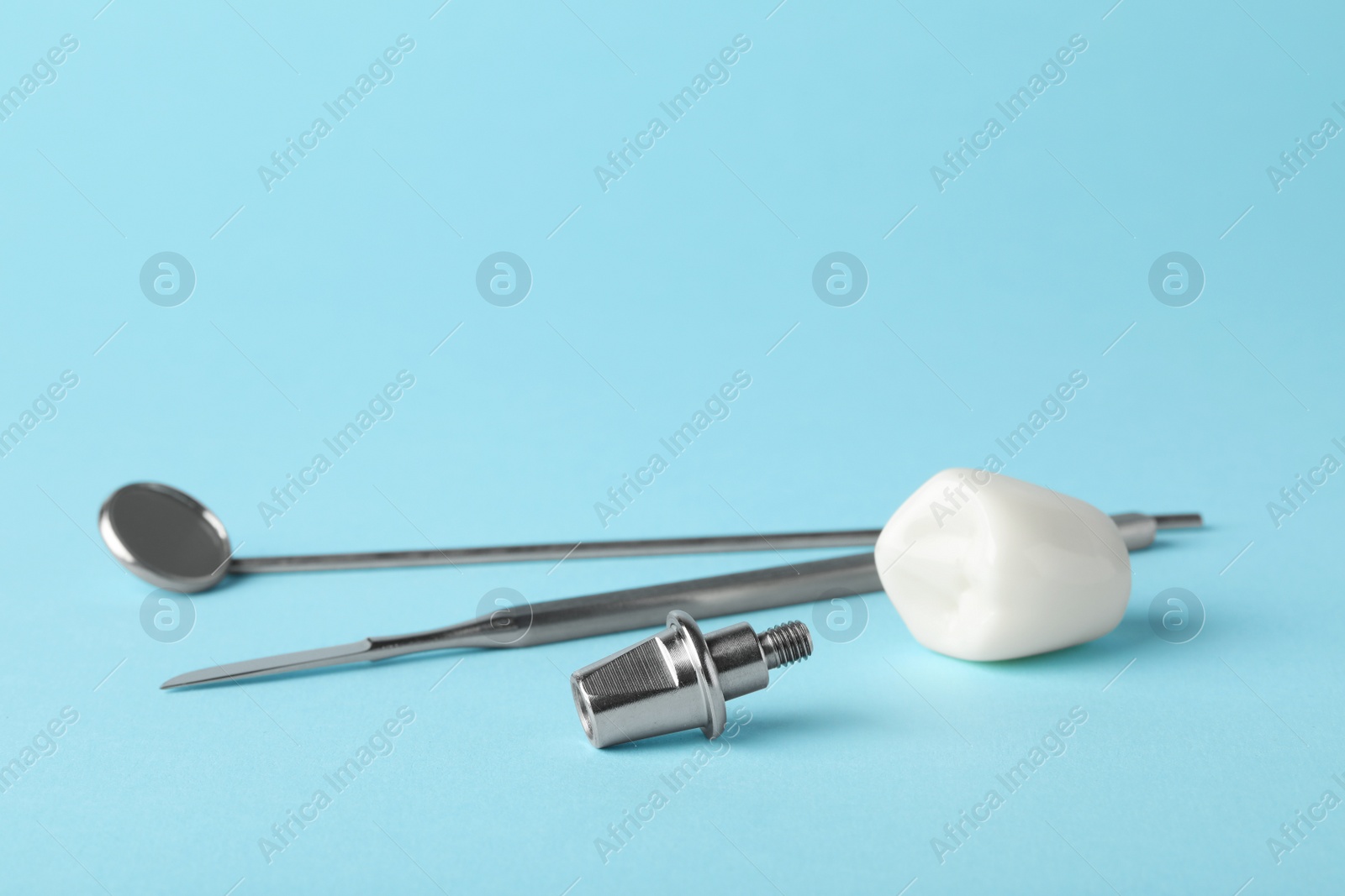 Photo of Abutment and crown of dental implant near medical tools on light blue background. Space for text