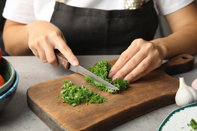 Photo of Woman cutting fresh green parsley on wooden board, closeup