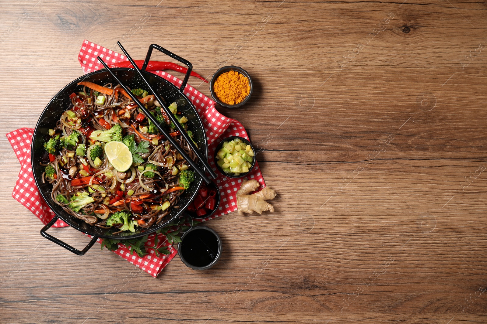 Photo of Stir-fry. Tasty noodles with meat in wok, chopsticks and ingredients on wooden table, flat lay. Space for text