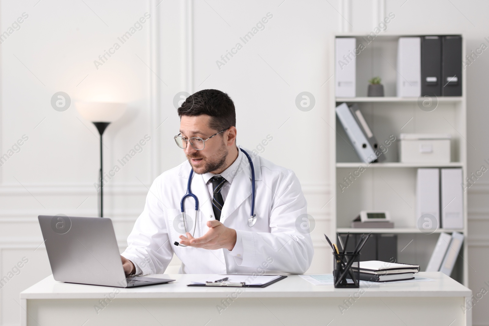 Photo of Doctor having online consultation via laptop at table in clinic