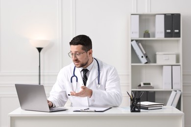 Doctor having online consultation via laptop at table in clinic