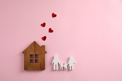 Photo of Figures of family, house and red hearts on pink background, flat lay. Space for text