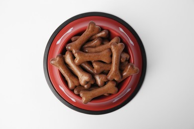 Photo of Red bowl with bone shaped dog cookies on white background, top view