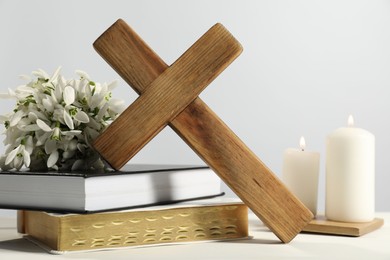 Photo of Wooden cross, ecclesiastical books, church candles and flowers on white table, closeup