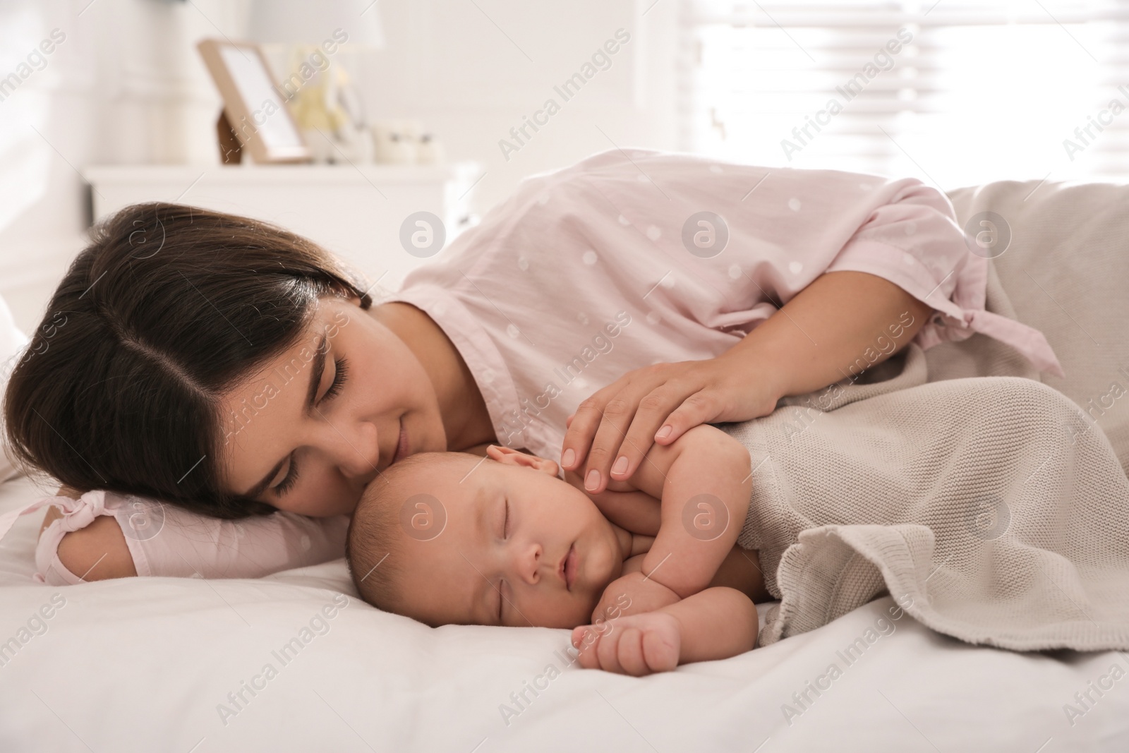 Photo of Young mother resting near her sleeping baby on bed at home