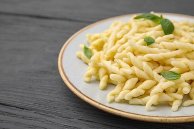 Photo of Plate of delicious trofie pasta with basil leaves on grey wooden table, closeup. Space for text