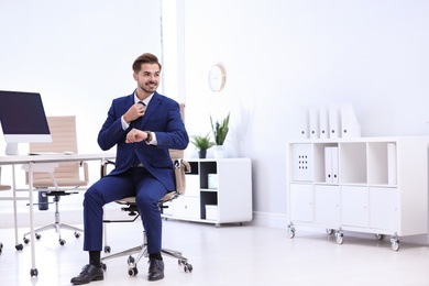Photo of Young businessman sitting on office chair at workplace, space for text