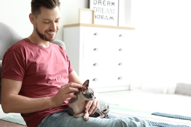 Photo of Young man with cute cat sitting on floor at home