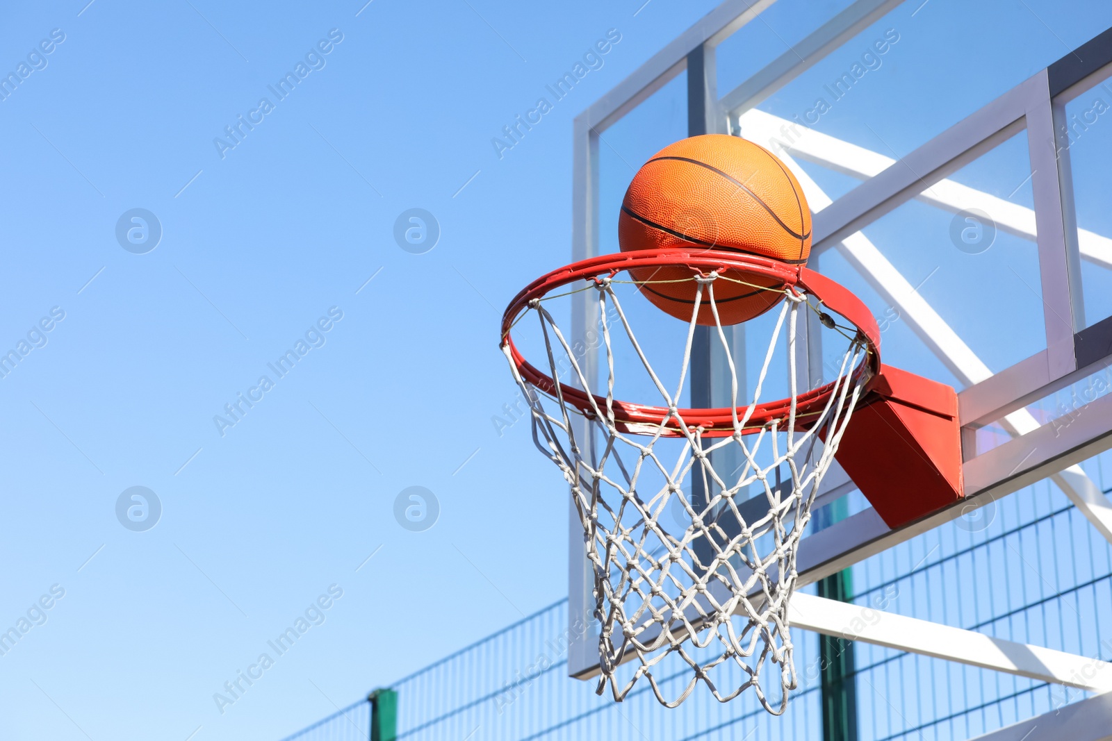 Photo of Basketball ball and hoop with net outdoors on sunny day